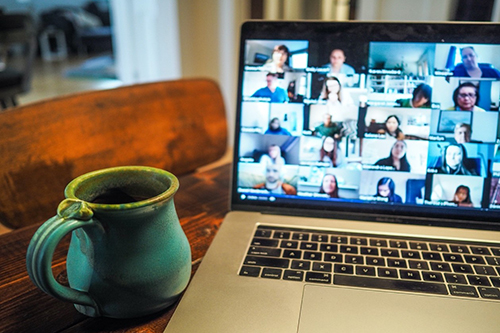 A zoom meeting displayed on a laptop next to coffee cup